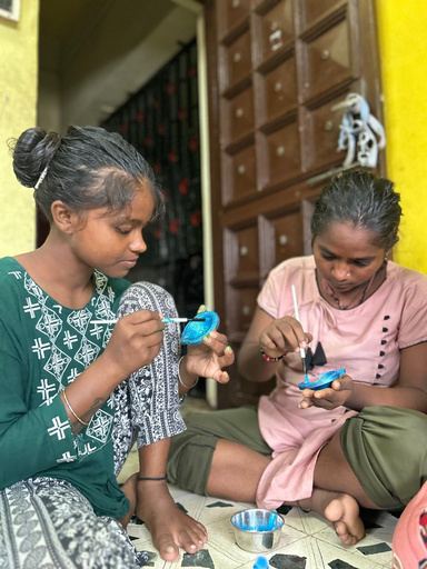 Two girls painting a craft item together.