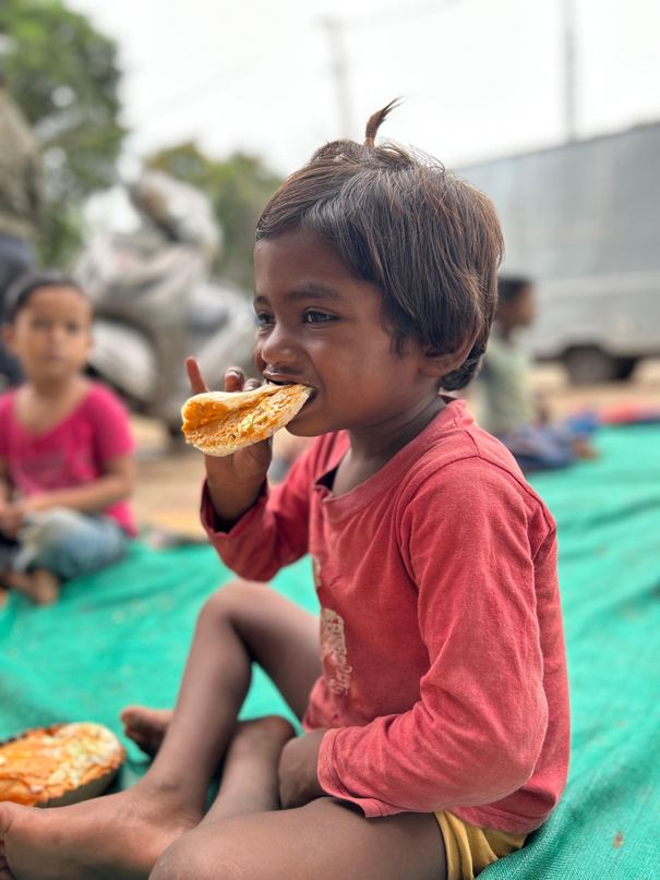 A young child eating a snack while sitting on a mat.
