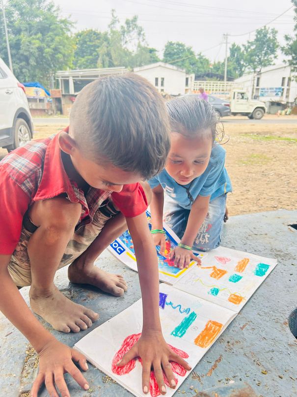 Two young boys painting on a sheet of paper.