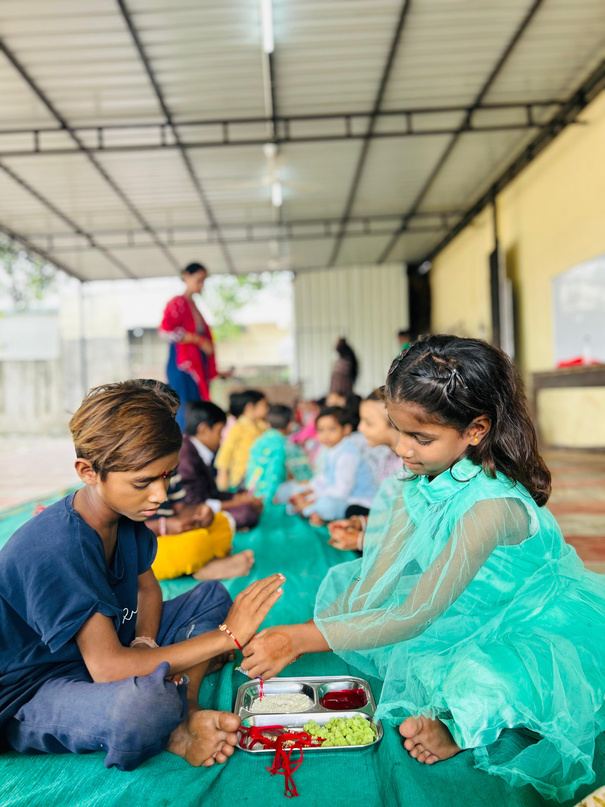 Children sitting together on mats in a covered learning space.