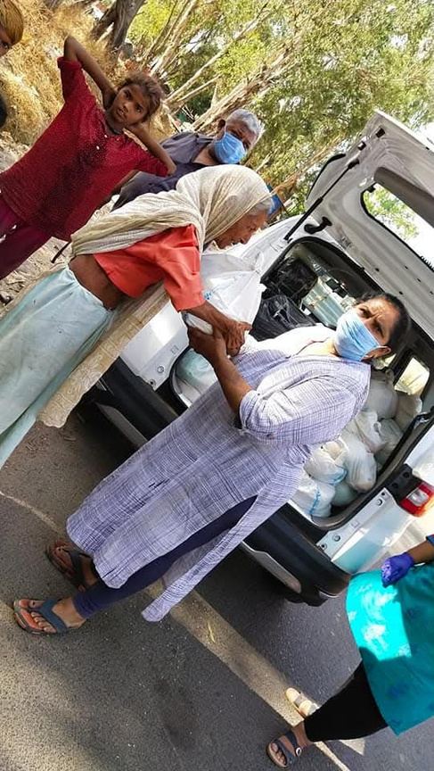 A volunteer in a mask unloading food packets from a car.
