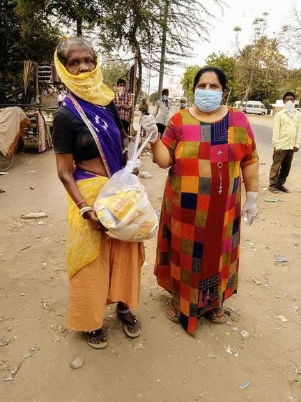 Two women in masks holding a bag of food supplies.
