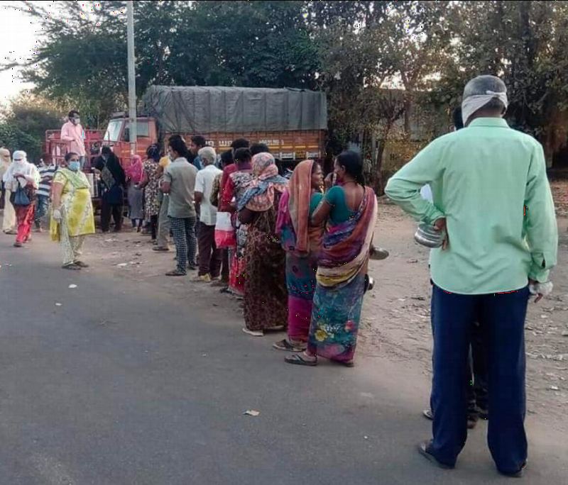 People standing in a line by the road during the pandemic.