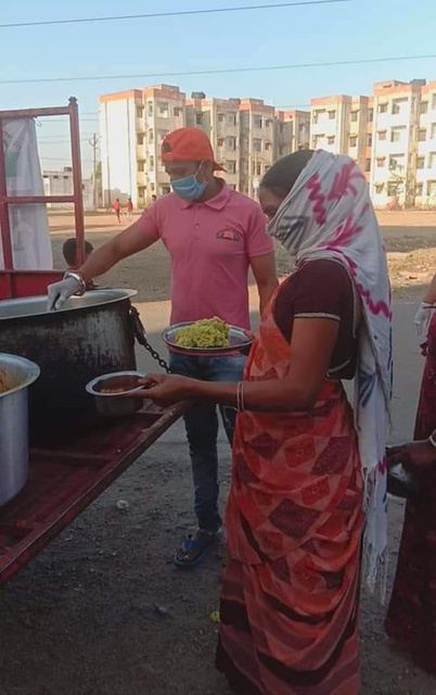 A volunteer in a mask serving food from a large pot.