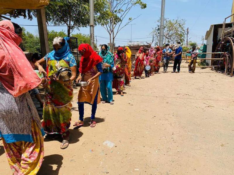 People in masks standing in a long, spaced-out line by the road.