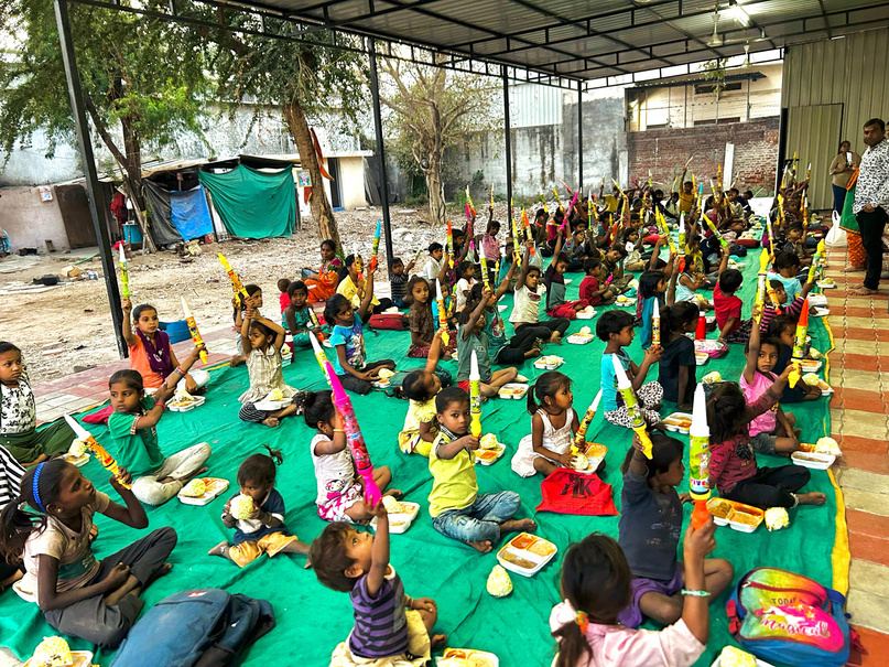 Many children seated in rows on mats, sharing a meal together.
