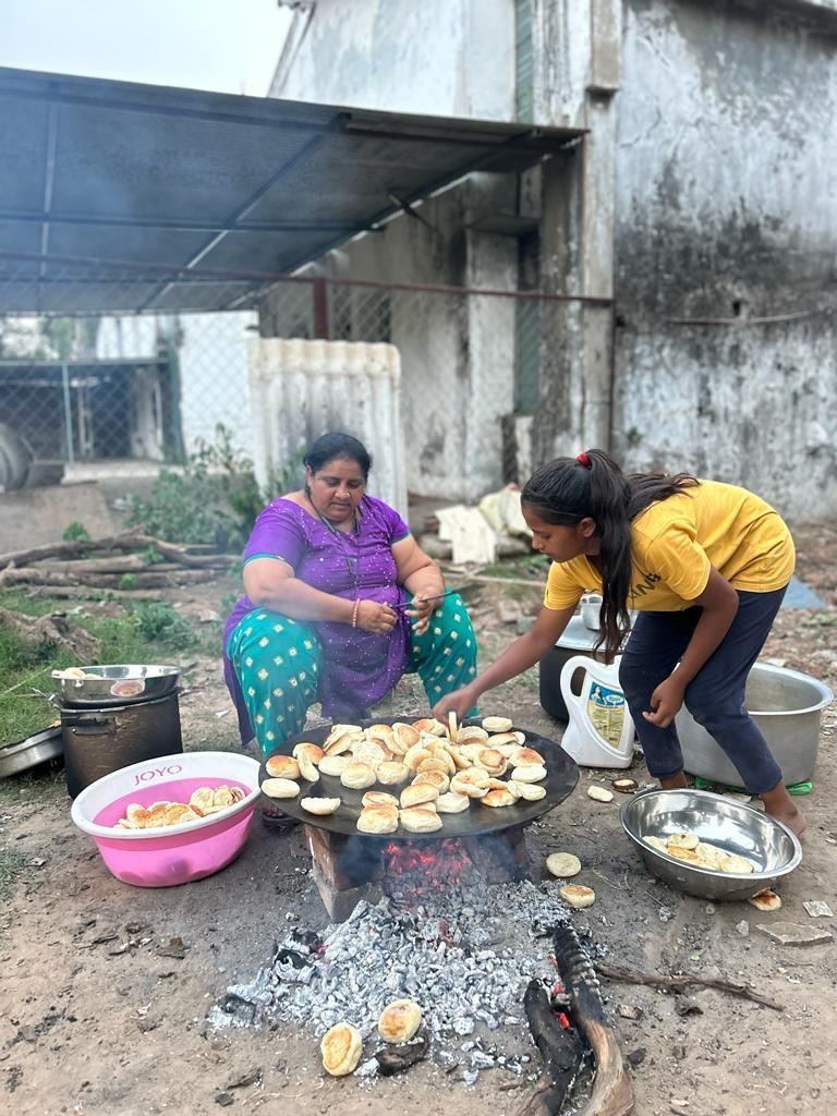 Two women cooking flatbread over an outdoor stove.