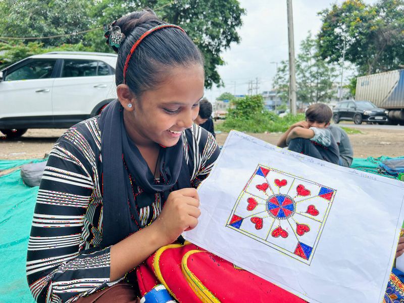 A girl smiling while colouring a pattern on paper.