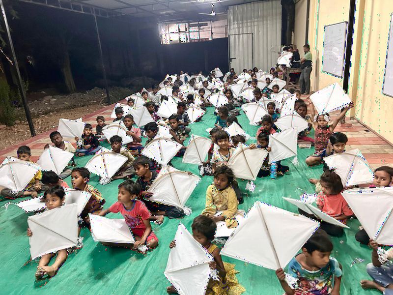Children sitting on mats with white kites in a large hall.