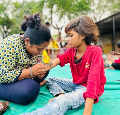 A volunteer applying mehendi to a girl's hand.