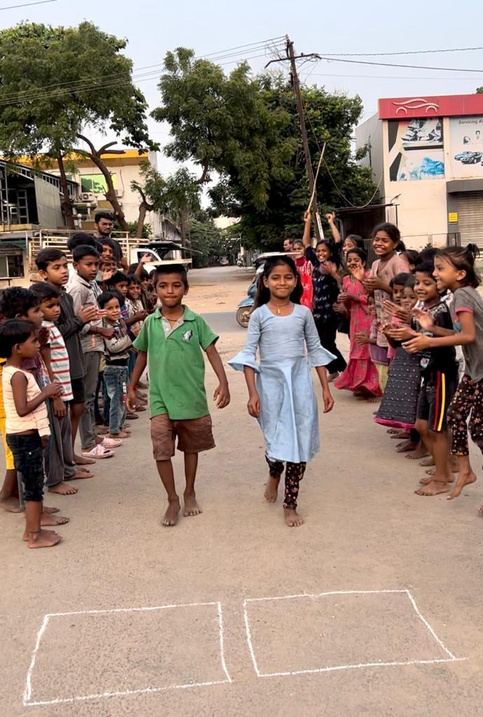 Children cheering as two classmates walk between them on the street.