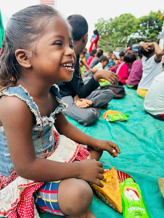 A little girl laughing while sitting with other children.
