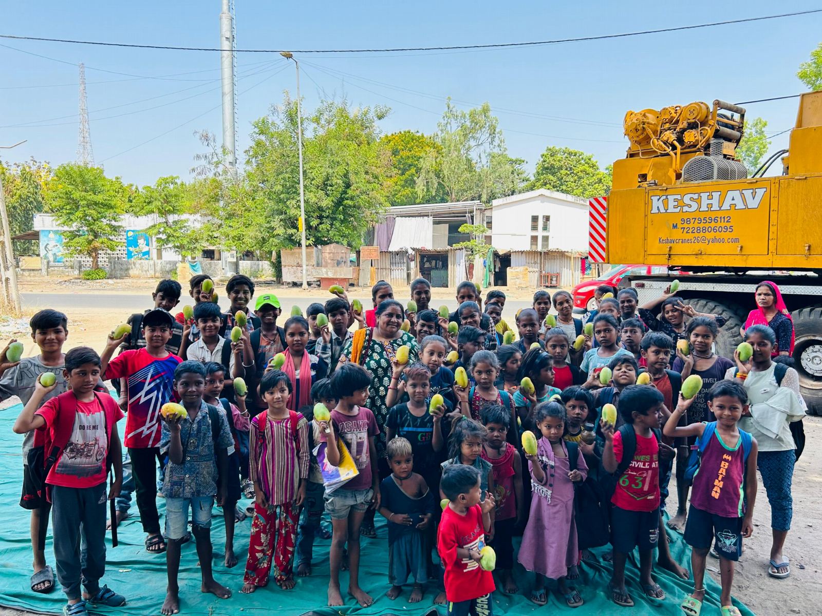 A large group of children gathered outdoors with Divyaroshni Foundation, smiling and holding items they received.