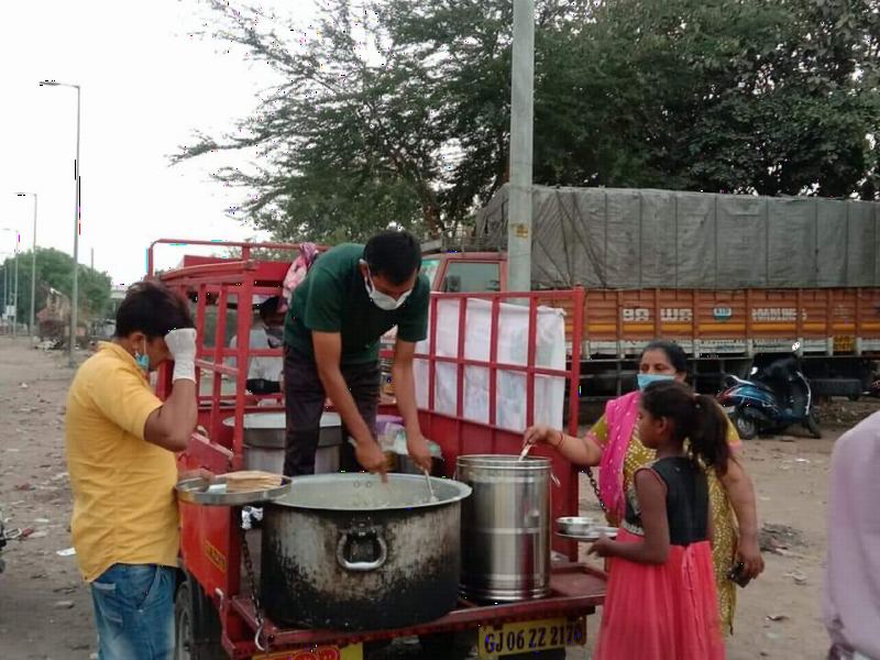 Volunteers serving cooked food from large pots by the roadside.
