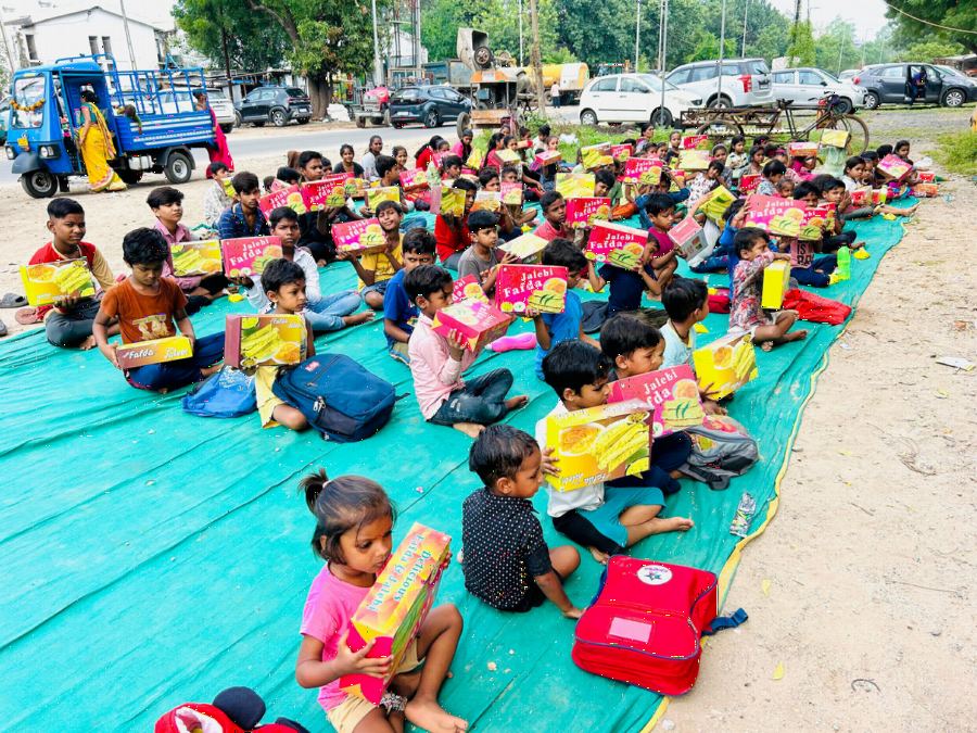Rows of children seated on mats holding new stationery kits and school bags.