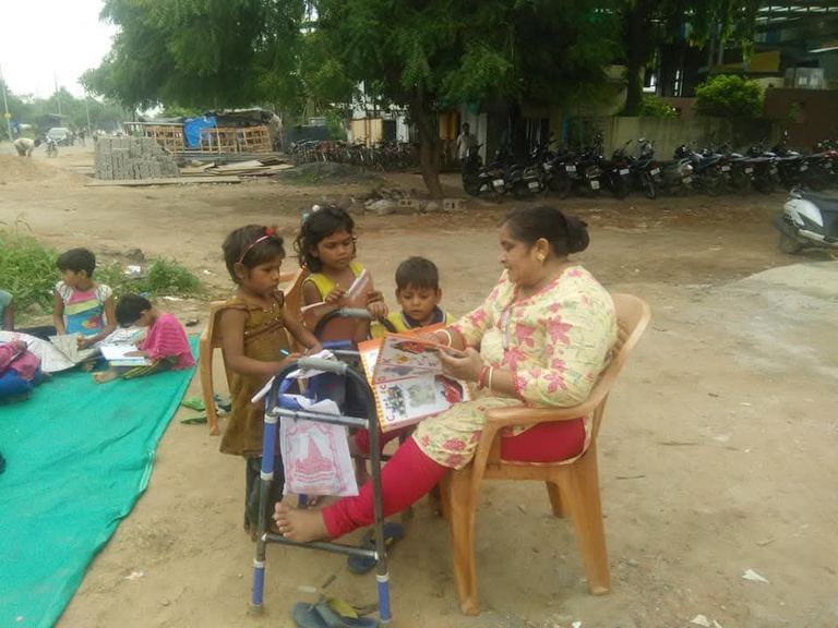 Children sitting on mats outdoors as a foundation volunteer helps them with their studies.