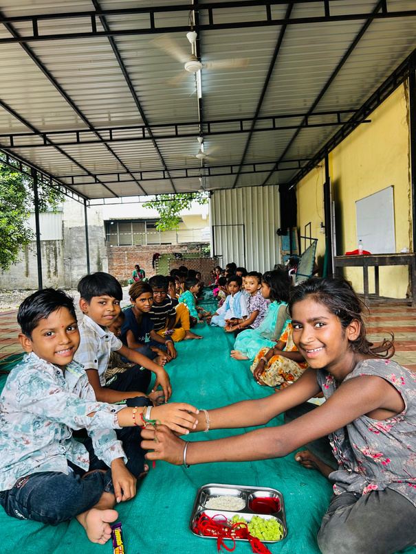 Children sitting together on mats in a covered learning space.