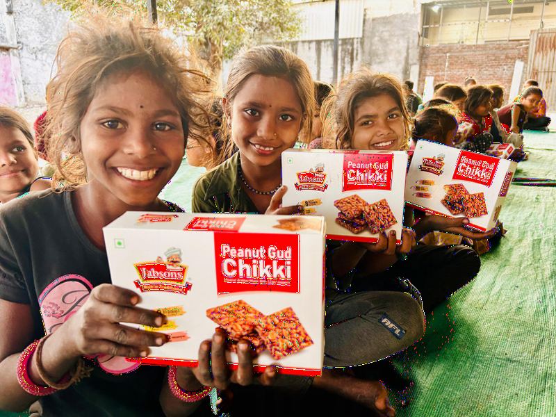 Smiling children holding boxes of chikki during Uttarayan.